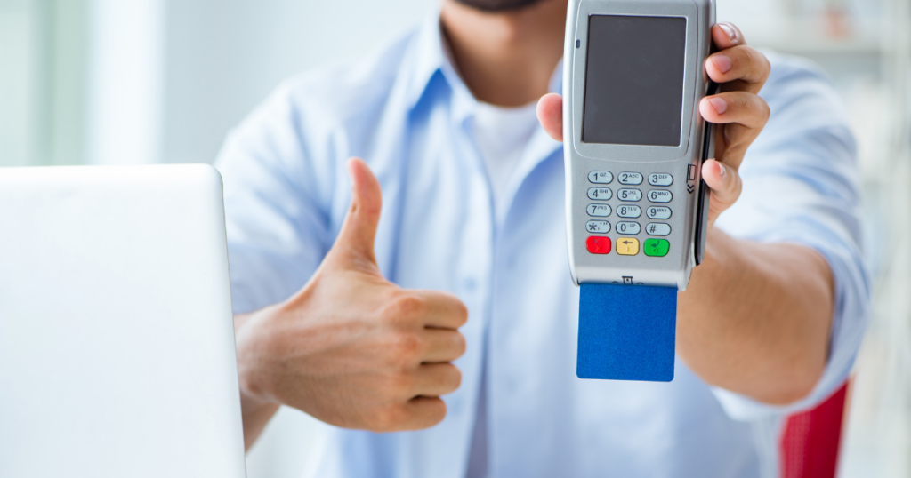 person holding a portable credit card terminal with a card inserted while giving a thumbs up